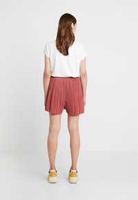Shorts plissés mi-cuisse en tissu rose poussiéreux, associés à un haut blanc à manches courtes. Portés avec des baskets épaisses de couleur claire.