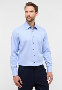 Camicia azzurro chiaro con bottoni neri, tasca sul petto e maniche lunghe. Tessuto liscio e design del colletto classico.