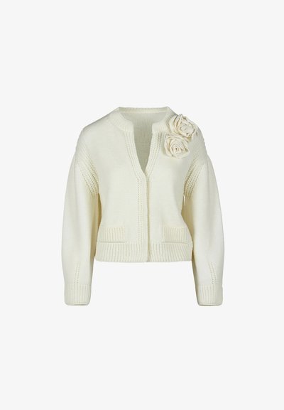 Kreminė megzta kardiganas su ilgomis rankovėmis, dviem priekinėm kišenėm, V formos iškirpte ir dviem dekoratyvinėm megztom gėlėm ant kairiojo peties.