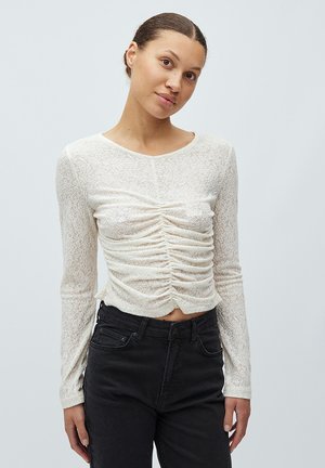 Top blanco de manga larga con diseño fruncido en la parte delantera, hecho de un tejido transparente y texturizado. Combinado con jeans negros ajustados.