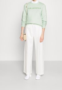 Sudadera verde menta con la marca "KARL LAGERFELD", combinada con pantalones anchos blancos de corte alto y zapatos blancos a juego. Pequeño bolso beige.