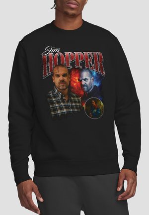 Schwarzer Sweatshirt mit einem bedruckten Design, das mehrere Bilder des Charakters "Jim Hopper" in verschiedenen Hintergründen und Farben zeigt.