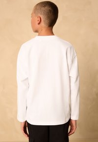 Langærmet hvid T-shirt med rund halsudskæring og løs pasform, lavet af blødt bomuldsstof. Har et enkelt, sømløst design på ryggen.