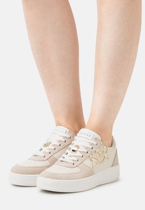 Beige Sneaker aus einer Mischung aus Wildleder und Leder mit strukturierter Oberfläche, weißer Sohle und goldenen Logo-Akzenten. Schnürung mit Perforationen.