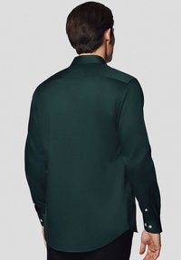 Ciemnozielona koszula z długim rękawem, charakteryzująca się gładką teksturą, guzikami na mankietach oraz klasycznym kołnierzykiem. Tył koszuli prezentuje dopasowany krój.