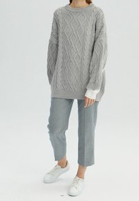 Lichtgrijze gebreide trui met kabelpatroon, oversized pasvorm en geribbelde manchetten. Gecombineerd met geruite, cropped broek en witte sneakers.