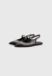 Black leather slingback shoes with pointed toes, adjustable strap, and flat soles. Smooth finish with a subtle sheen. Minimalistic design.