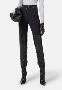 Leggings neri con vita alta realizzati in un tessuto liscio e dettagli con zip, abbinati a stivali alti fino alla coscia in nero lucido con effetto coccodrillo.