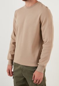 Felpa beige a maniche lunghe con finitura testurizzata e polsini a costine, abbinata a pantaloni cargo verde oliva. Design semplice con collo a giro.