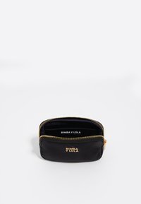 Bolsa de cuero negro con cremallera dorada. El interior cuenta con la marca y un compartimento para tarjetas. Textura suave, forma ovalada compacta.