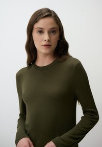 Maglione a maglia color verde oliva scuro, con scollatura rotonda e maniche lunghe con polsini a coste. Texture morbida e design aderente.