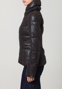 Giacca a vento nera con finitura lucida, colletto alto e motivo trapuntato. Presenta una tasca con zip e un dettaglio brandizzato sulla manica.