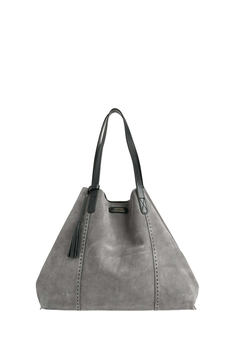 Sac fourre-tout en suède gris avec des poignées en cuir noir, présentant une finition texturée, un pompon décoratif et des coutures sur les côtés.