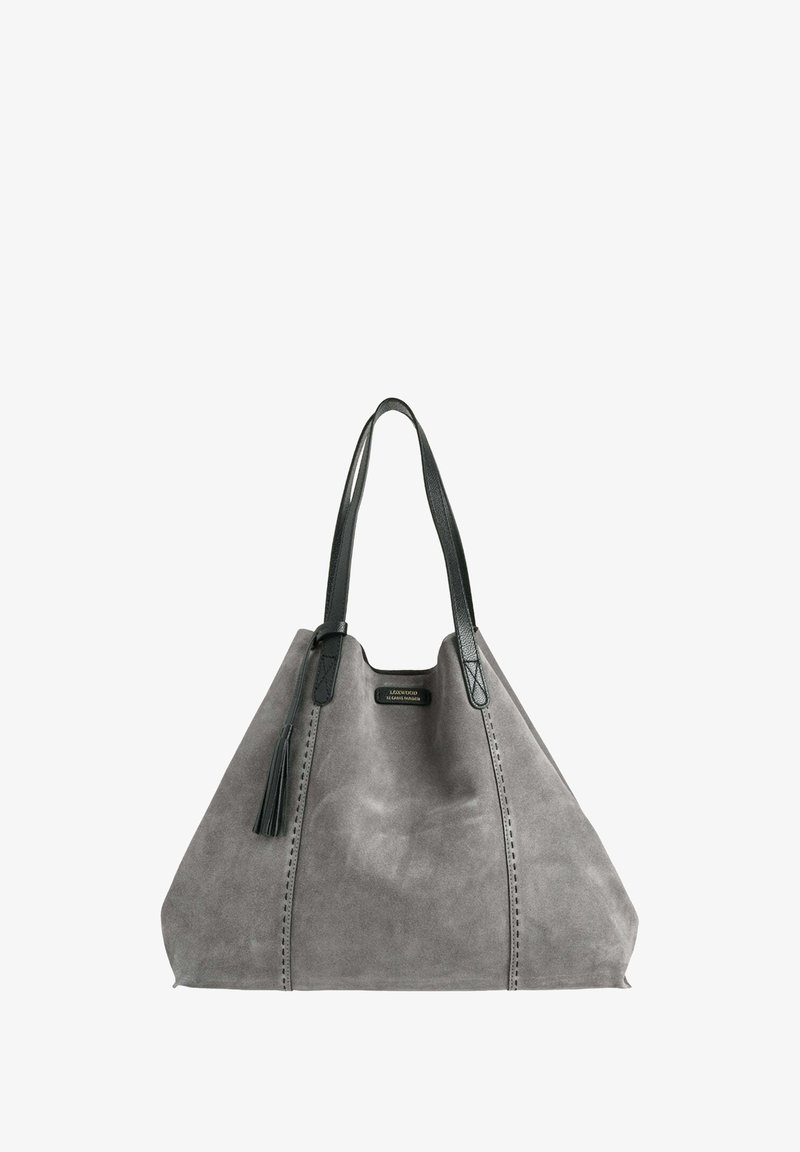 Sac fourre-tout en suède gris avec des poignées en cuir noir, présentant une finition texturée, un pompon décoratif et des coutures sur les côtés.