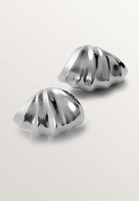 Objetos decorativos metálicos plateados en forma de conchas con bordes ondulados, que presentan superficies lisas y estrías, sobre un fondo claro.