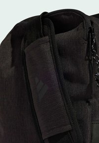 Musta reppu, jossa on teksturoitu kangas, varustettuna vetoketjukiinnityksellä, mustilla hardware-osiolla ja hillityllä logotuksella. Kestävä ja toiminnallinen muotoilu.