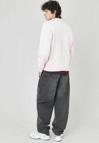 Pull rose clair texturé avec des poignets côtelés, associé à un jean ample gris foncé. Chaussures : baskets blanches.