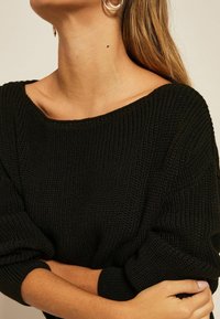 Pull noir en tricot avec un large col et des manches longues légèrement surdimensionnées. Tissu texturé avec des poignets côtelés.