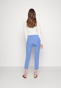 Ljusblå tapered byxor med en slät textur, som har en midjehög midja och fotlång längd, kombinerade med en långärmad krämfärgad topp.