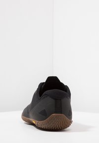 Czarne buty sportowe z plecionym wierzchem z materiału tekstylnego, gumową podeszwą z teksturowanym gripem i wzmocnionym piętą. Minimalistyczny design bez wzorów.