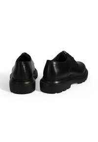 Schwarze Lederschuhe mit runder Spitze, dicke schwarze Gummisohle und Schnürdesign. Glatte Oberfläche ohne sichtbare Muster oder Akzente.