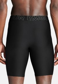Black compression shorts made of textured material. Features a wide waistband with "UNDER ARMOUR" in prominent lettering.
