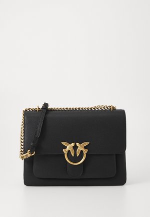 Schwarze Ledertasche mit strukturiertem Finish, goldenem Kettenriemen und einzigartigem hardware Akzent in Form eines Vogels auf dem vorderen Klappenverschluss.