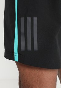 Pantalones cortos deportivos negros con acentos en teal, que cuentan con tres franjas verticales negras, fabricados con tejido ligero y de textura suave.