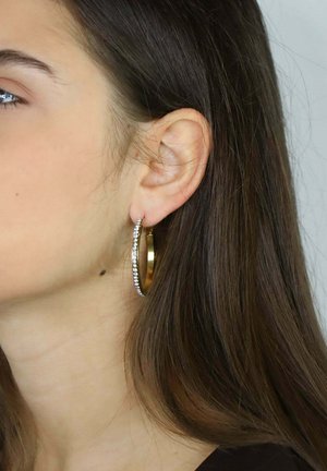 Orecchini a cerchio dorati con finitura lucida, caratterizzati da una fila di strass trasparenti lungo un bordo, che mostrano un design circolare liscio.