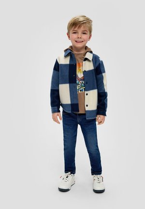 Blauw en wit geblokte fleece shirtjack, bruin graphic t-shirt, blauwe jeans en witte sneakers met zwarte accenten.