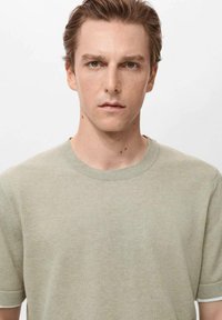 Tricou scurt, de culoare verde deschis, dintr-un material moale, cu guler rotund și o textură netedă, având detalii de cusătură discrete.