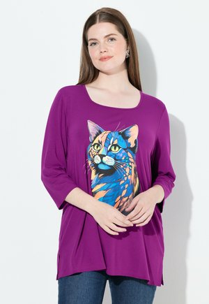 Purple loose-fitting top with 3/4 sleeves, featuring a colorful cat graphic print on the front. Soft, stretchy fabric with side slits.