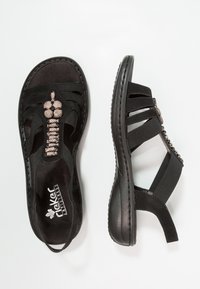 Czarne sandały z elastycznymi paskami i dekoracyjnymi metalowymi akcentami. Płaska podeszwa z wyściółką, z kwiatowym wzorem na wierzchu.