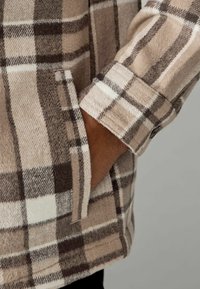 Rutig flannel skjorte i neutrale farver. Har et brunt og off-white ternet mønster, blødt tekstur, standard manchet med knapdetalje.