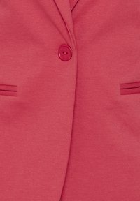 Blazer rose avec une fermeture à un seul bouton, texture douce et deux poches avant avec un détail de couture subtil.