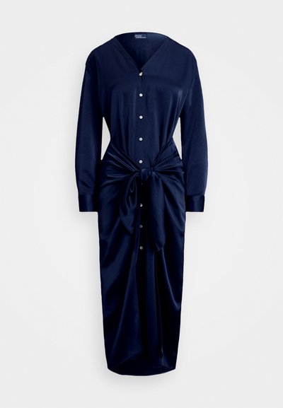 Jūras zila kleita, kas izgatavota no gludas auduma, ar V veida kakla izgriezumu, pogu priekšpusi, garām piedurknēm un mezgla vidukļa detaļu, ar plūstošu svārku.