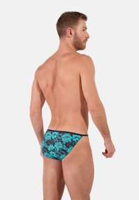 Männer Schwimmbriefe mit einem floralen Muster in Türkis und Marineblau. Der Stoff ist weich mit einer engen Passform und hebt ein tief sitzendes Design hervor.
