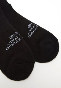 Calzini neri in cotone con texture a coste e logo stampato bianco vicino alla caviglia. Il design è semplice, senza motivi o colori aggiuntivi.