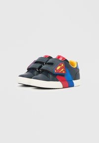 Sötétkék gyerek sportcipő piros és kék részletekkel, két tépőzáras pánttal és szuperhős logóval az oldalon. Fehér talp.