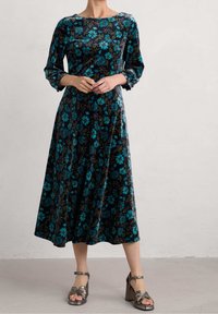 Langärmliges Kleid aus schwarzem Samt mit floralen Mustern in Türkis und grünen Akzenten, fließender Silhouette und rundem Ausschnitt.