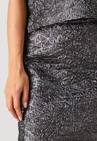 Hand rust opzij van een metalen, gestructureerde zwart-zilveren rok met een bijpassend bovenstuk zichtbaar bij de taille.