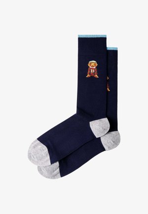 Calcetines hasta la pantorrilla azul marino con dedos y talones gris claro, puño azul claro y una pequeña figura bordada con ropa roja y naranja cerca de la parte superior.