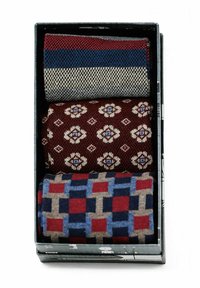 Drei Stoffrollen in einer schwarzen Box: ein gestreiftes Design in Rot, Blau und Creme; ein Blumenmuster in Rot und Beige; und ein geometrisches Muster in Blau, Rot und Beige.