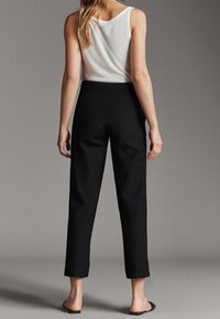 Zwarte op maat gemaakte broeken met een slim fit, verkorte lengte en een gladde textuur, gecombineerd met een witte mouwloze top. Eenvoudig ontwerp, strakke lijnen.