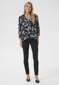 Blumenbluse in Marineblau mit weißen und hellgrauen Blumen; V-Ausschnitt, lockere Passform und ¾-Ärmel. Kombiniert mit engen schwarzen Jeans.