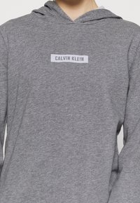 Felpa grigia realizzata in morbido cotone misto, con tasca a marsupio frontale e un'etichetta rettangolare bianca con la scritta "CALVIN KLEIN."