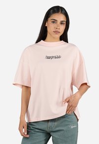 Lyserosa oversized t-skjorte med rund hals, korte ermer og brodert "Propagand"-logo i svart sentrert på brystet.