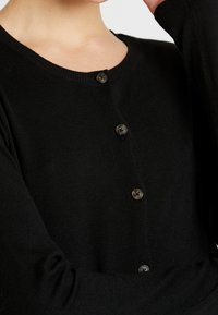 Svart kofta i stickat tyg, med rund halsringning och framknappar, med en jämn yta och långa ärmar.