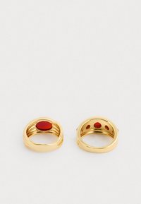 Zlaté prstene s výrazným červeným kameňom; jeden má hladký oválny tvar, druhý má kruhové výrezy a akcentový kameň.