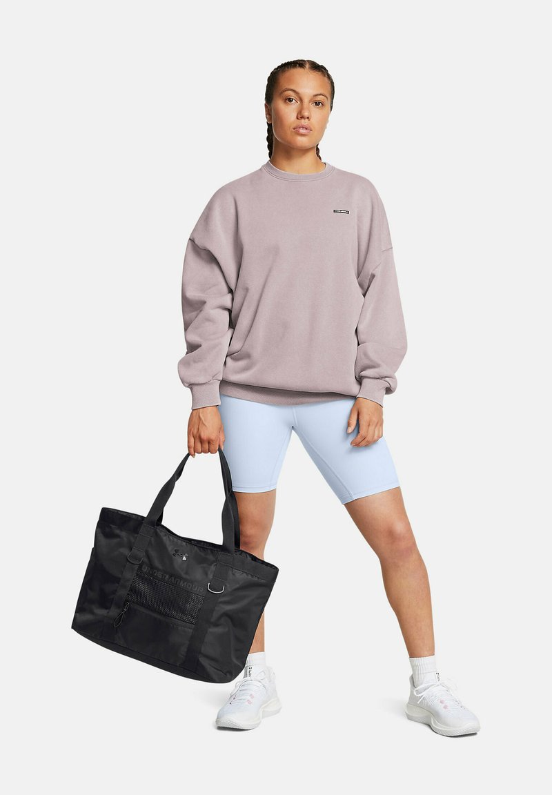 Sweat-shirt oversized violet clair, associé à un short de vélo bleu clair. Sac fourre-tout noir avec poches en maille et logo. Chaussures de sport blanches.